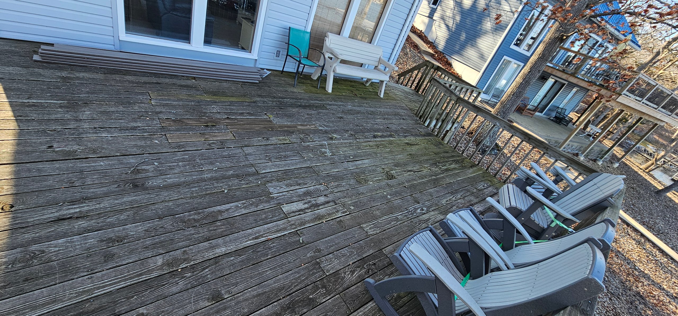 Weathered wooden deck with white and teal chairs near a house