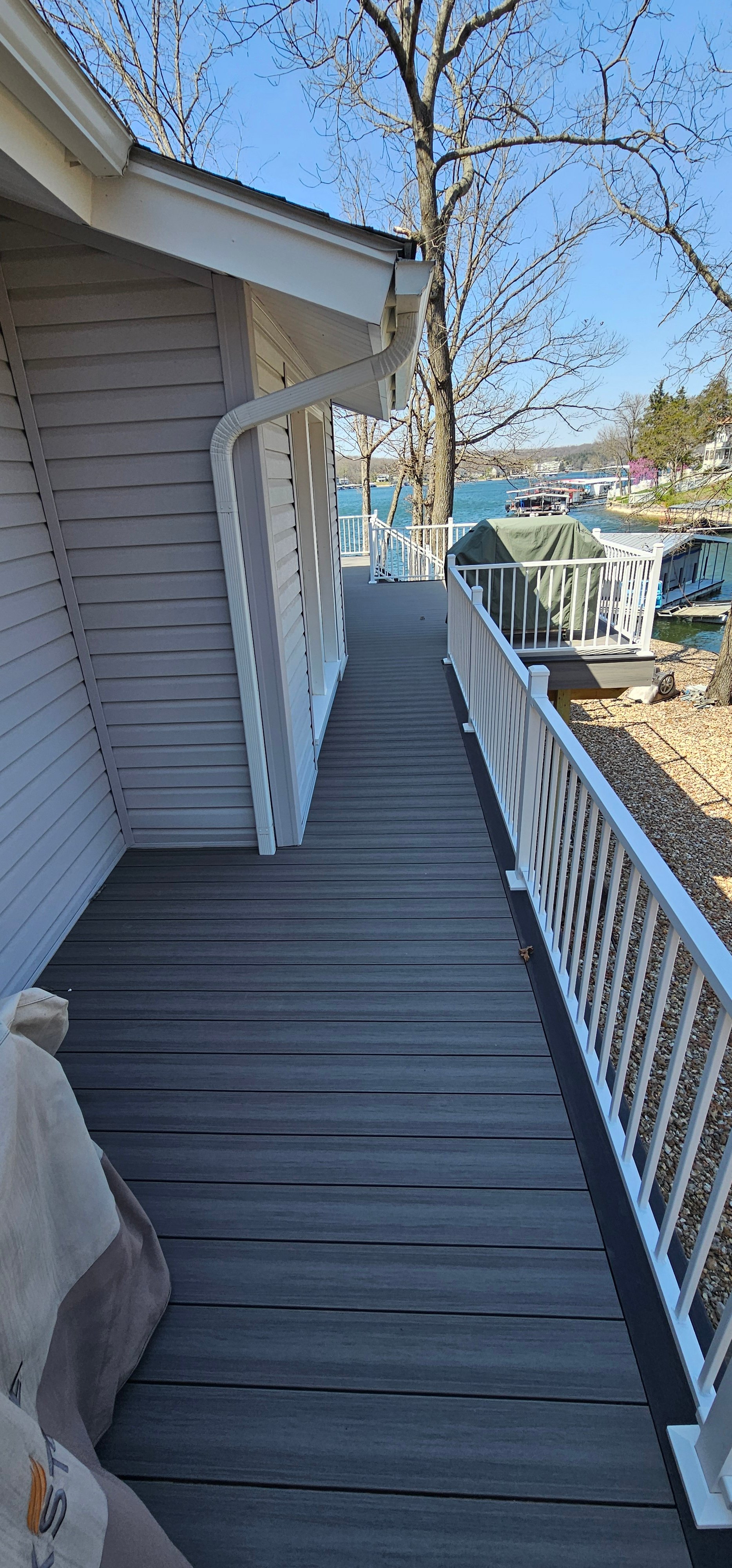 Wooden walkway along lake house with white railings and boat dock view