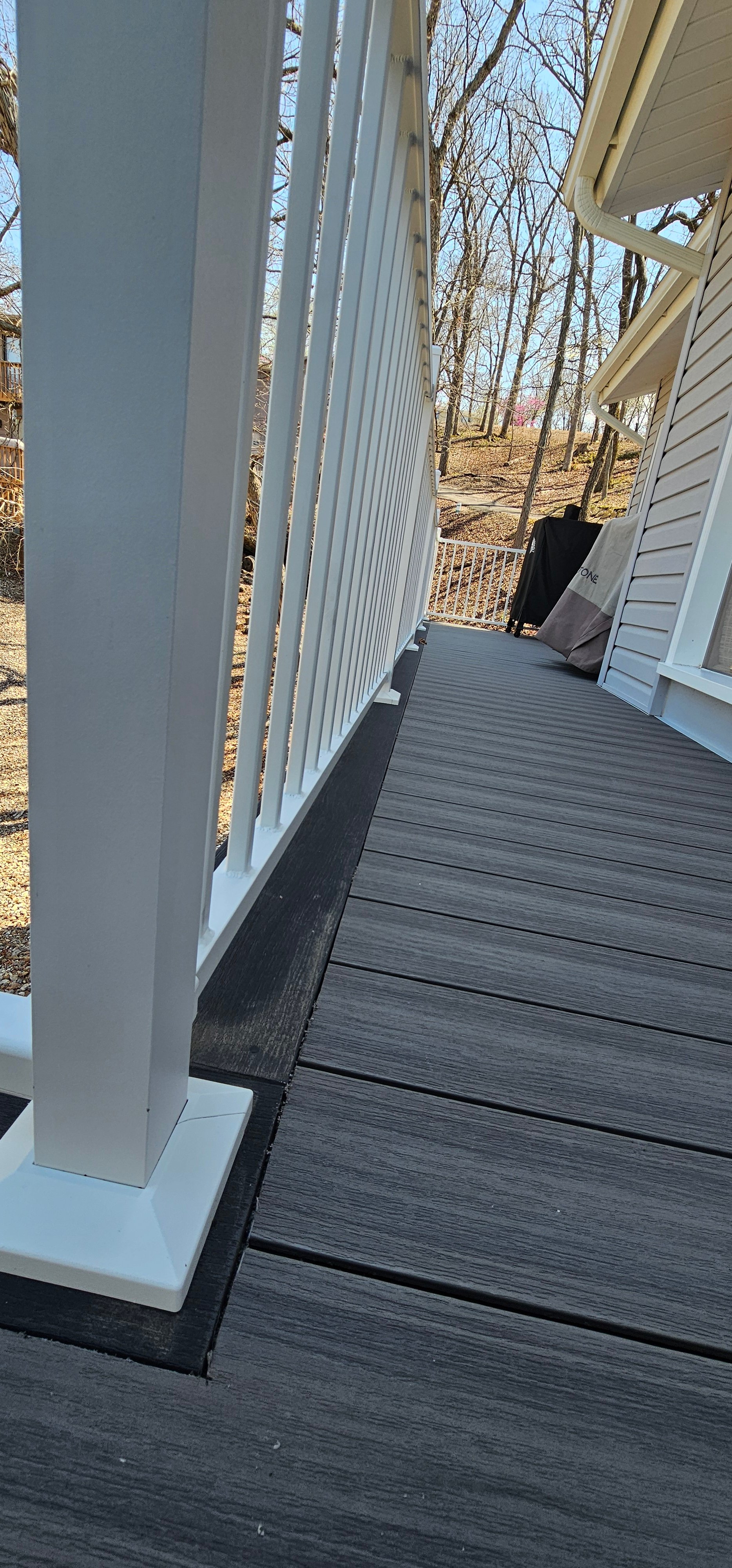 Gray wooden deck with white columns, trees in background on sunny day