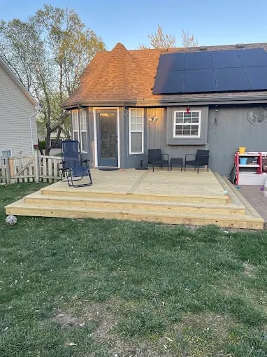Gray house with new wooden deck, solar panels, and backyard landscape
