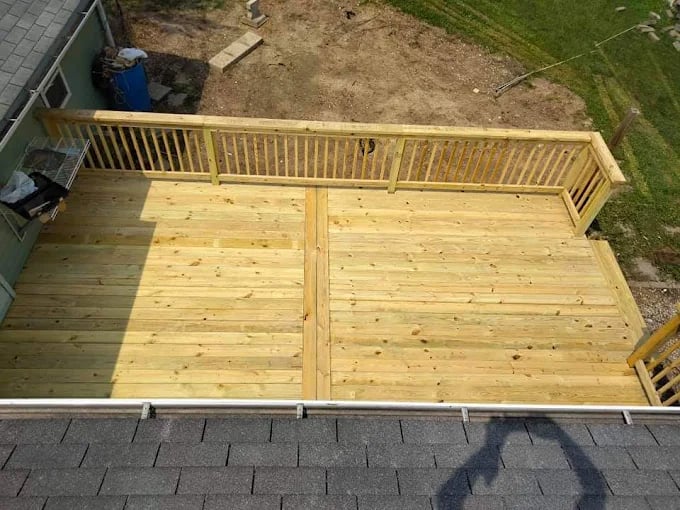 Newly constructed wooden deck with railing, attached to house over roof shingles