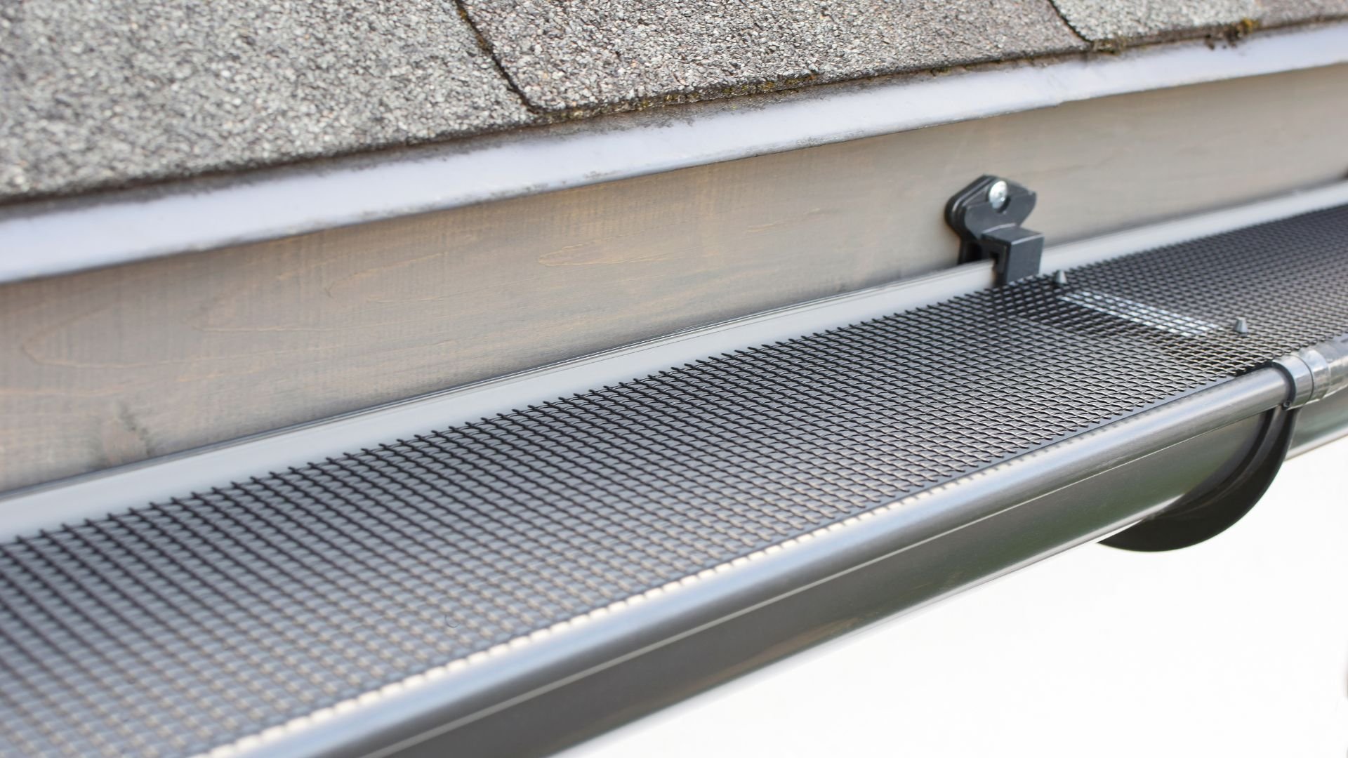 Gutter guard with mesh screen installed on roof edge near shingles