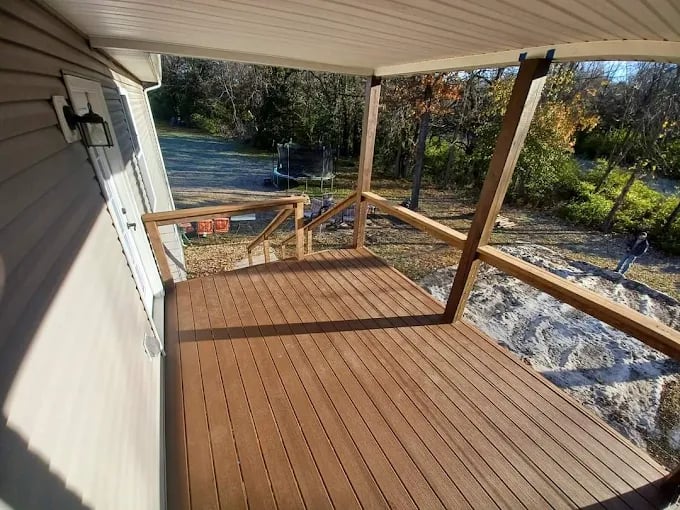 Wooden deck with railing overlooking a backyard with trees and gravel