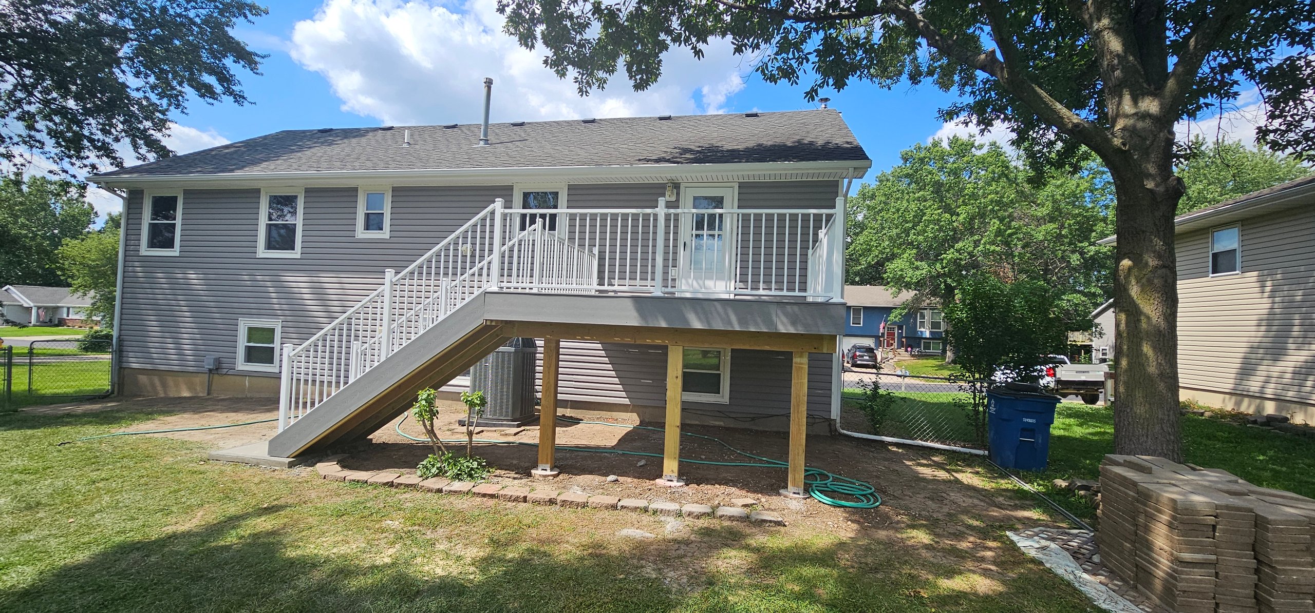 Two-story house with white deck and wooden support beams on sunny day