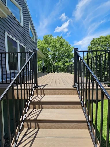 Wooden deck with black metal railings leading to a gray house on sunny day