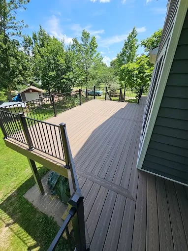 Spacious wooden deck with metal railings next to green house and trees