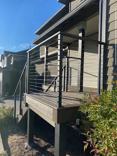 Modern wooden deck with metal railing attached to gray house