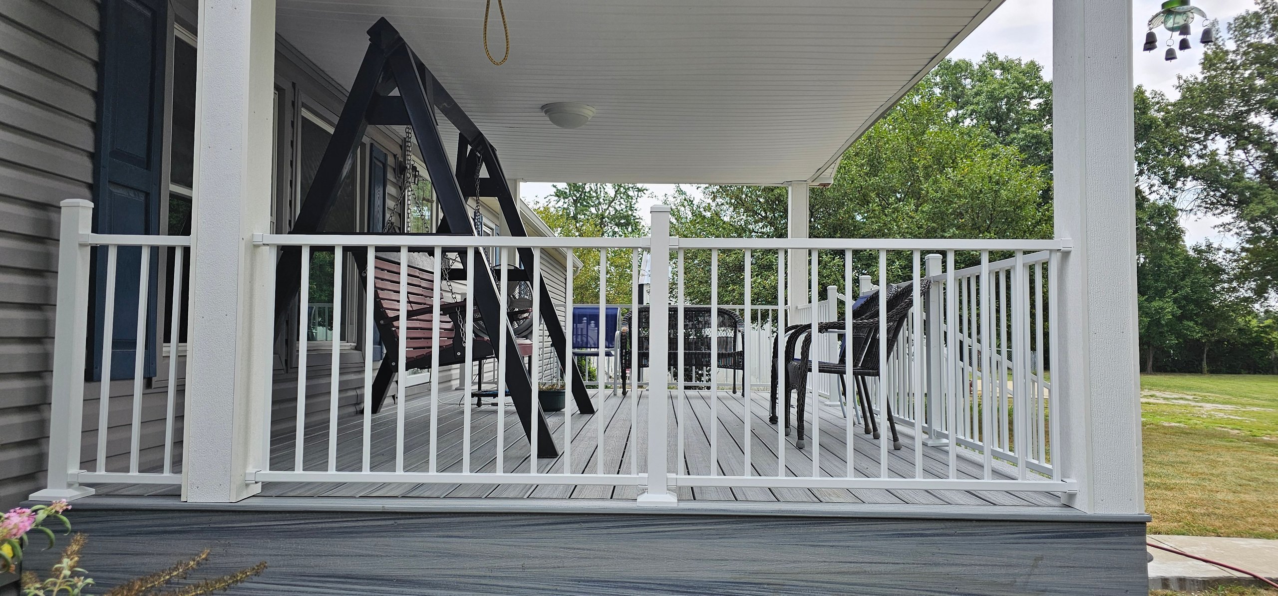 White-railed porch with wooden deck overlooking green lawn and trees
