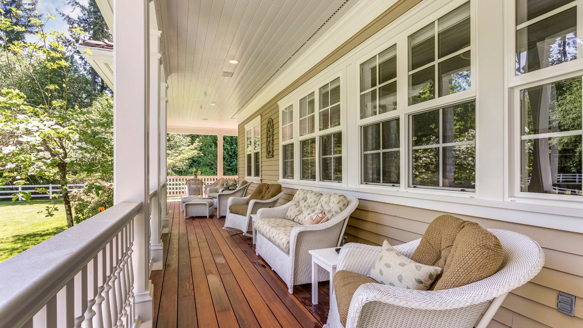Cozy wooden porch with white wicker chairs overlooking green trees