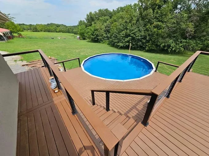 Round blue swimming pool on wooden deck surrounded by green grassy backyard