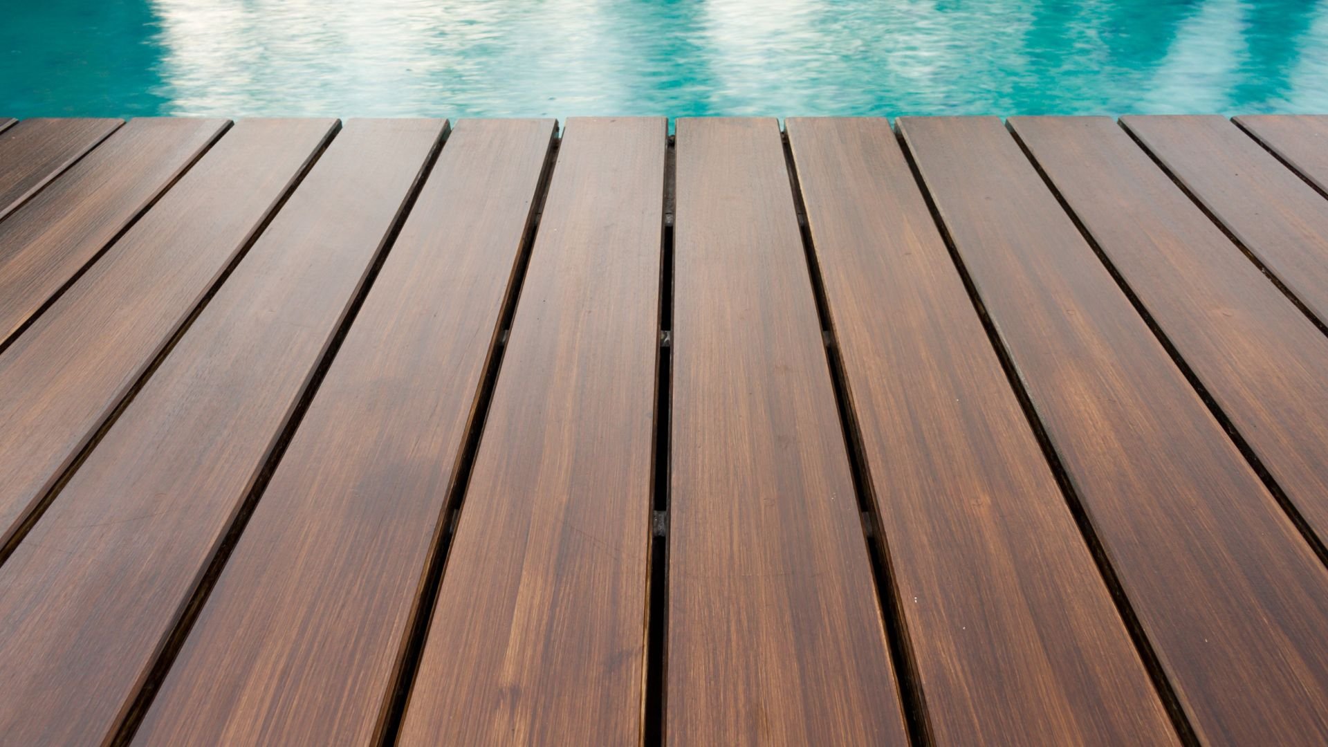 Wooden deck with turquoise swimming pool water in background